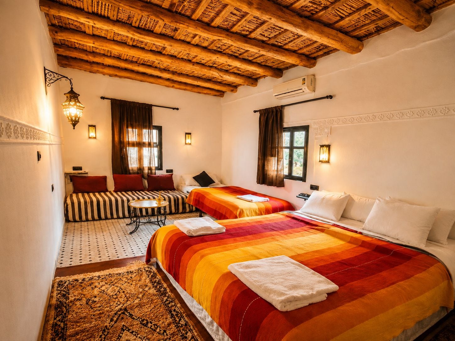 Una habitación de hotel con techo de madera, dos camas, un sofá, una mesita y un tapete estampado.
