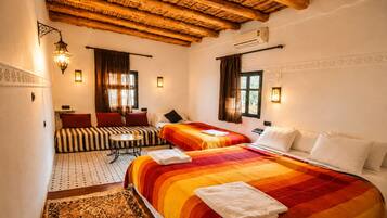 Una habitación de hotel con techo de madera, dos camas, un sofá, una mesita y un tapete estampado.
