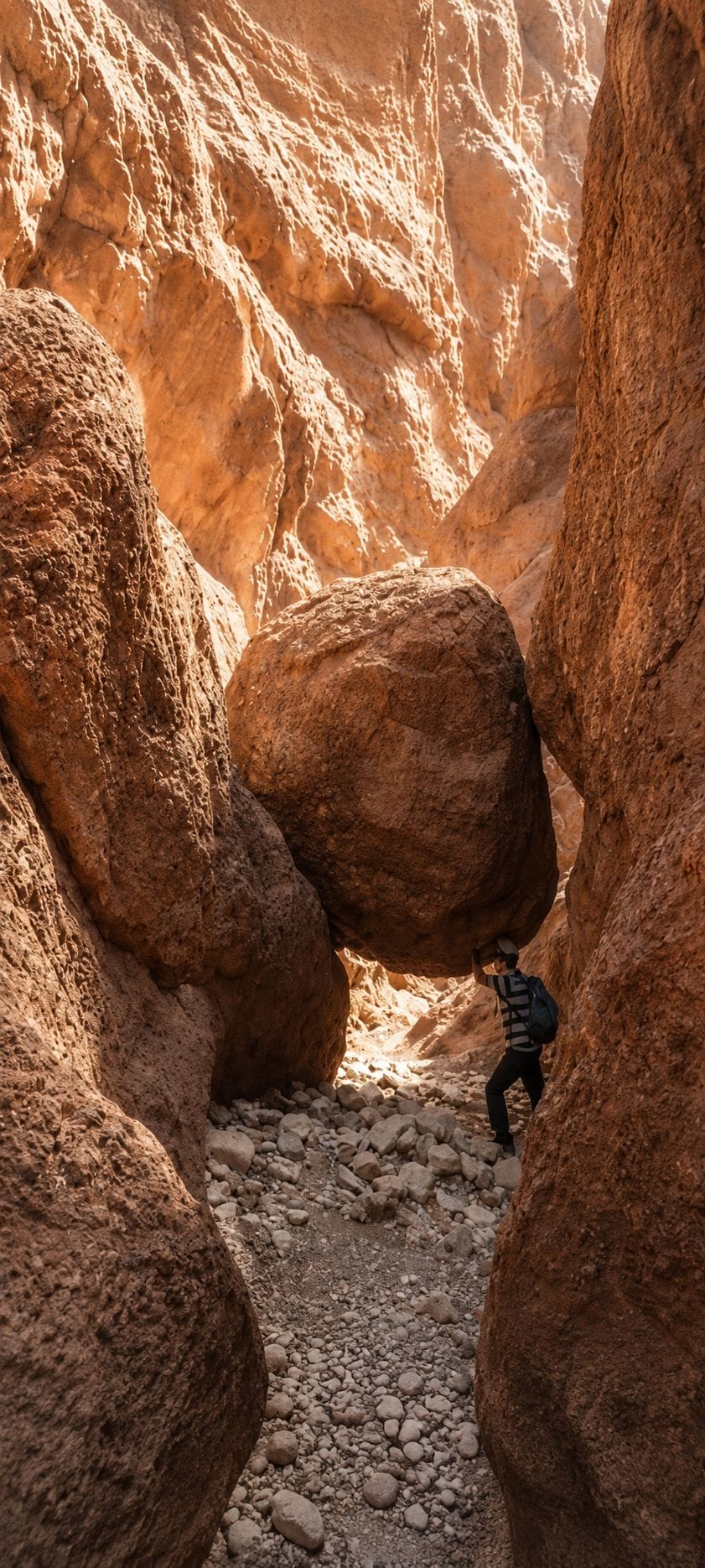 Un canyon étroit, parsemé de gros rochers, et une personne se tenant entre eux.