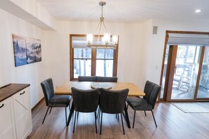 Un coin repas comprenant une table en bois, quatre chaises, un lustre et une grande fenêtre donnant sur un paysage agréable.