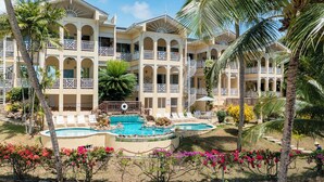 Ein Hotel mit mehreren Balkonen, einem zentral gelegenen Pool und tropischer Bepflanzung.