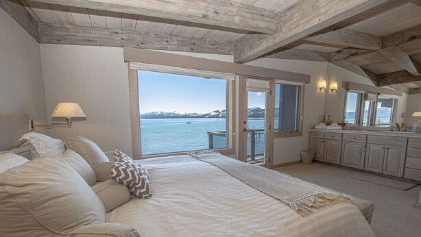 Ein Schlafzimmer mit einem großen Bett, Blick auf das Wasser und einer Holzbalkendecke.