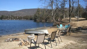 A lakeside campsite with a boat, chairs, and a fire pit.