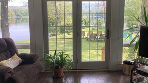 A room with a large sliding glass door leading to a backyard with a lawn, chairs, and a view of a lake.
