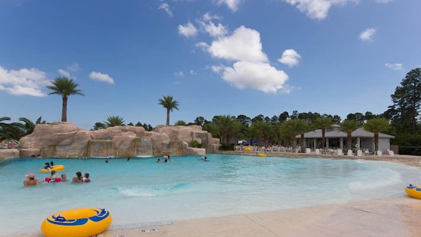 Una piscina con formaciones rocosas, palmeras y un pabellón.