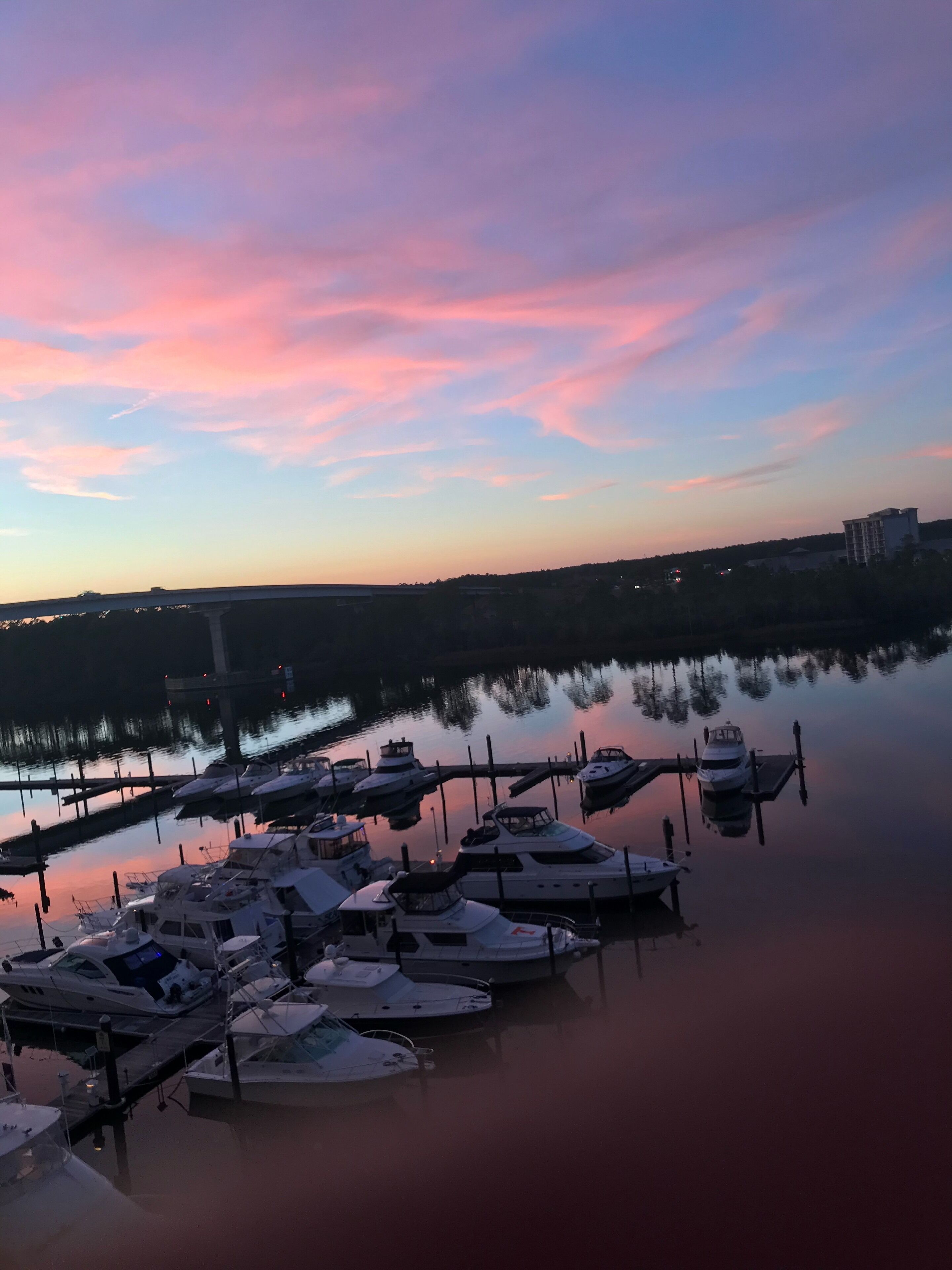 A marina with boats docked at the pier, surrounded by calm water reflecting the sky.