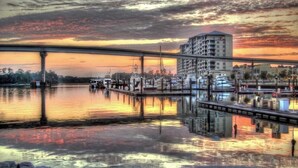 Marina frente al agua con un puente, barcos y un rascacielos reflejado en el agua durante el atardecer.