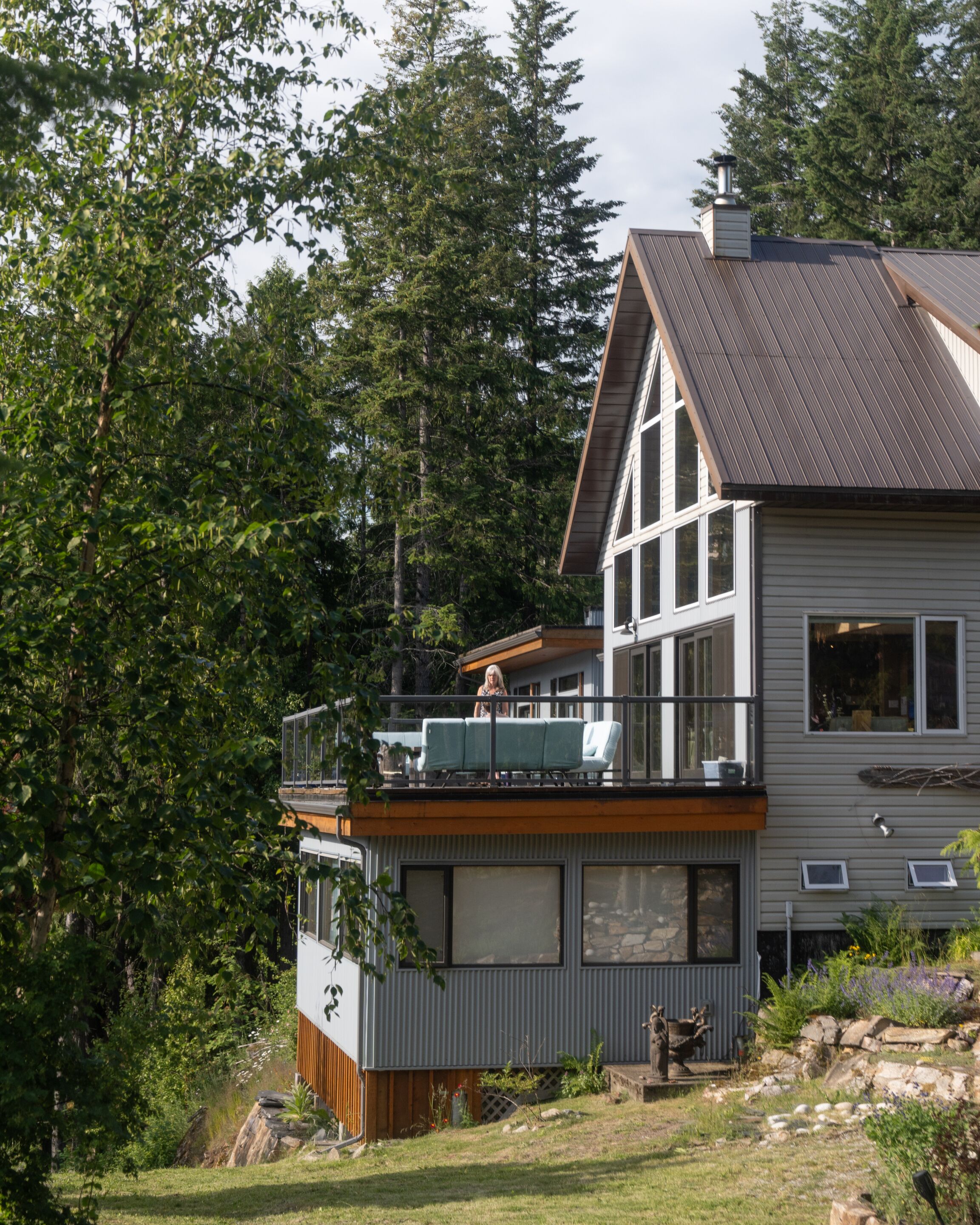 A modern two-story house with a balcony, large windows, and a stone foundation.