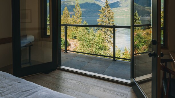 A bedroom with a large sliding glass door leading to a balcony with a mountain and lake view. - The Sentinel (Kaslo)