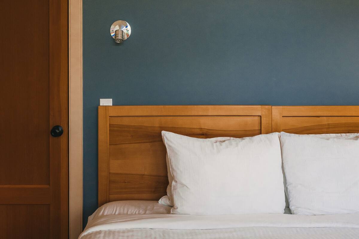Un dormitorio con cabecera de madera, una cama con ropa de cama blanca y una puerta a la izquierda.