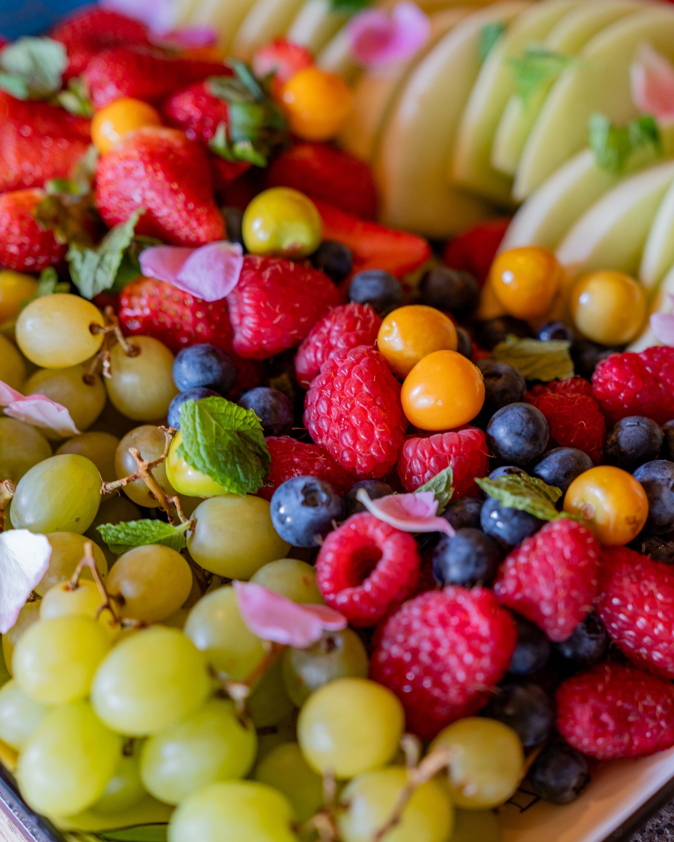 Un plateau de fruits variés comprenant des raisins, des fraises, des framboises, des myrtilles et des tranches de kiwi.
