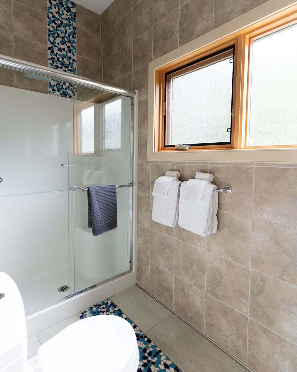 A bathroom with a glass shower enclosure, a toilet, and a window above the sink.