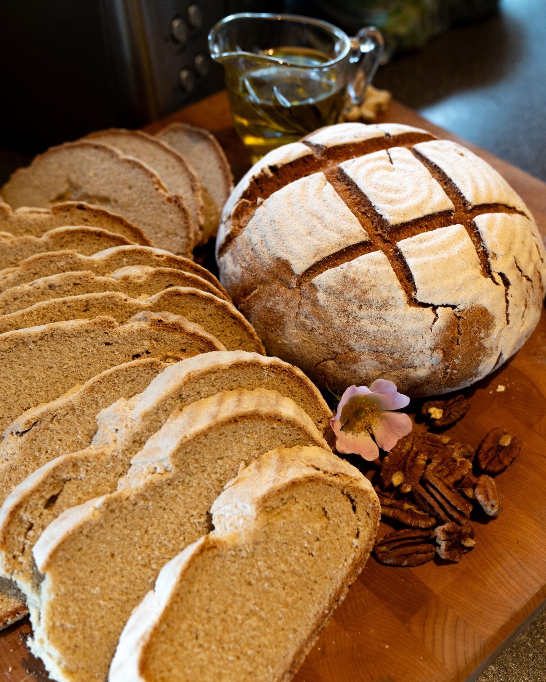 Une miche de pain décorée d’une croix sur le dessus, des tranches de pain et des noix de pécan sur une planche à découper en bois.