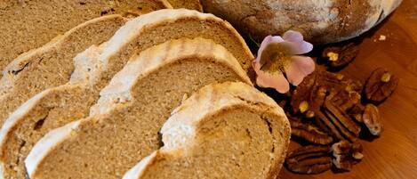 Une miche de pain décorée d’une croix sur le dessus, des tranches de pain et des noix de pécan sur une planche à découper en bois.