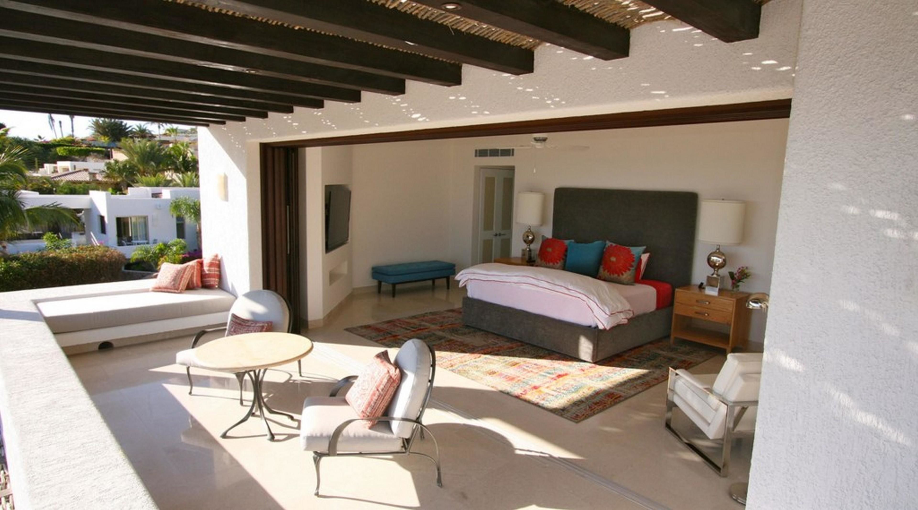 A modern bedroom with a large bed, a sitting area with a sofa and chairs, and a balcony with a view of the surrounding area.