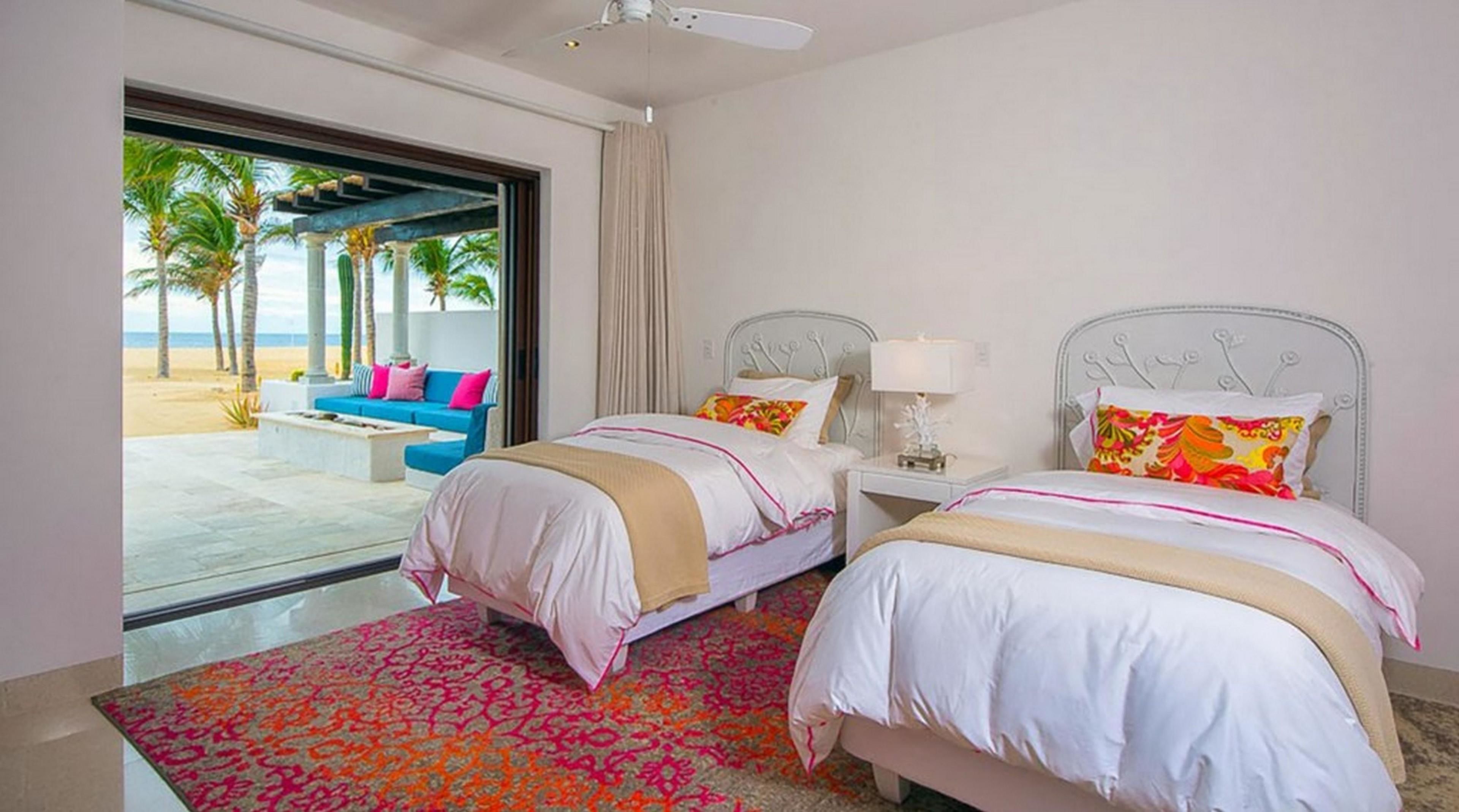 A hotel room with two beds, a view of the beach, and a balcony with a blue sofa.