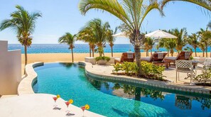 Ein Poolbereich mit einem geschwungenen Pool, Liegestühlen und Blick auf Strand und Meer.