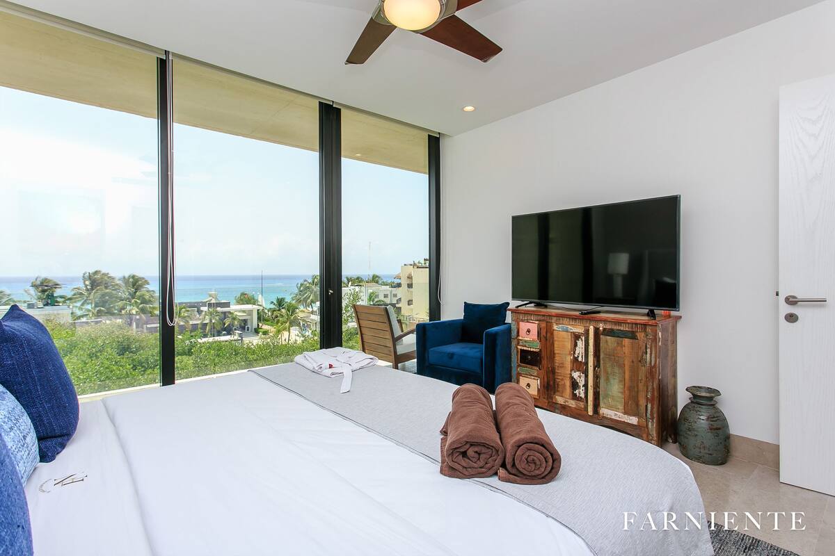 A modern hotel room with a large bed, a television, and a view of the ocean.