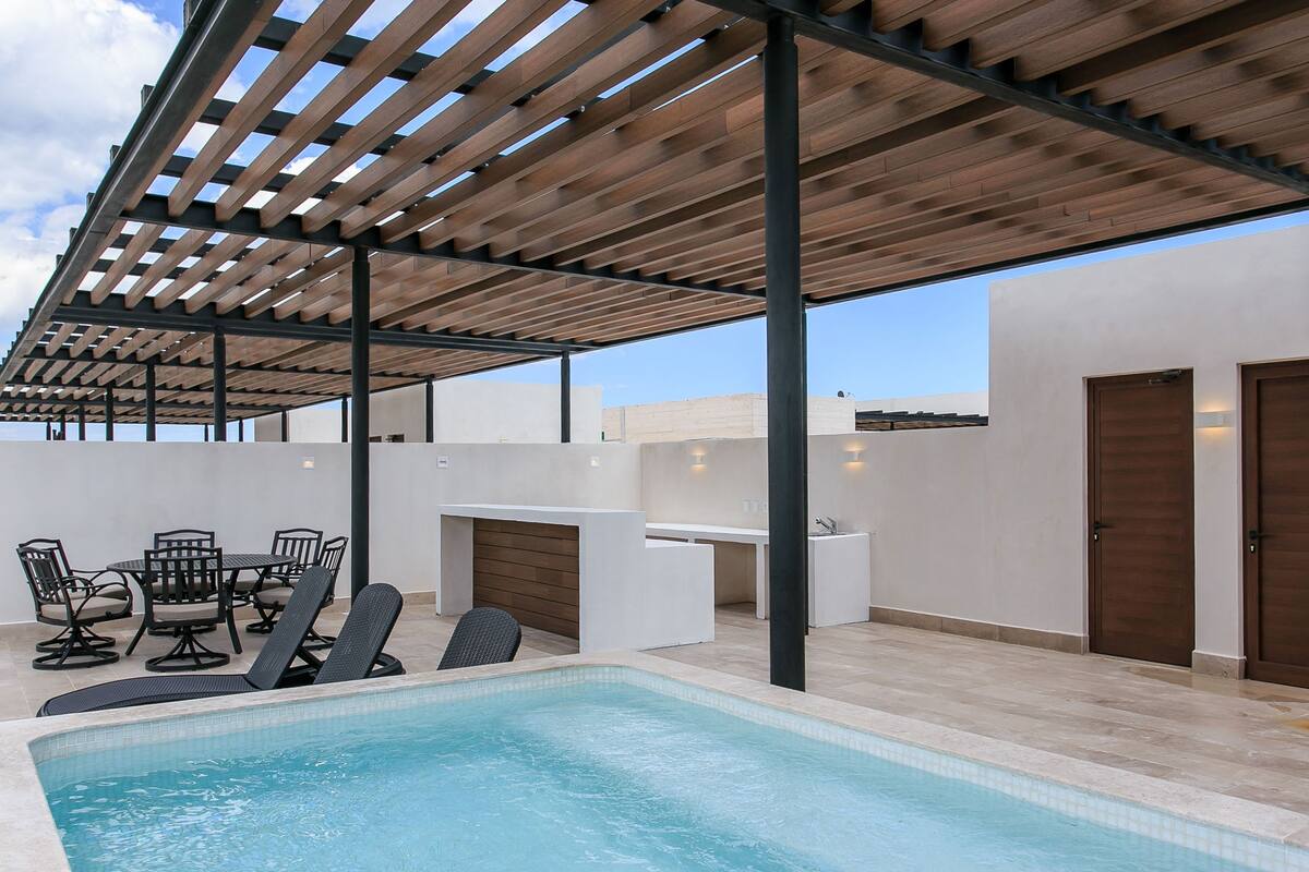 A pool area with a pergola, outdoor seating, and a small kitchen area.