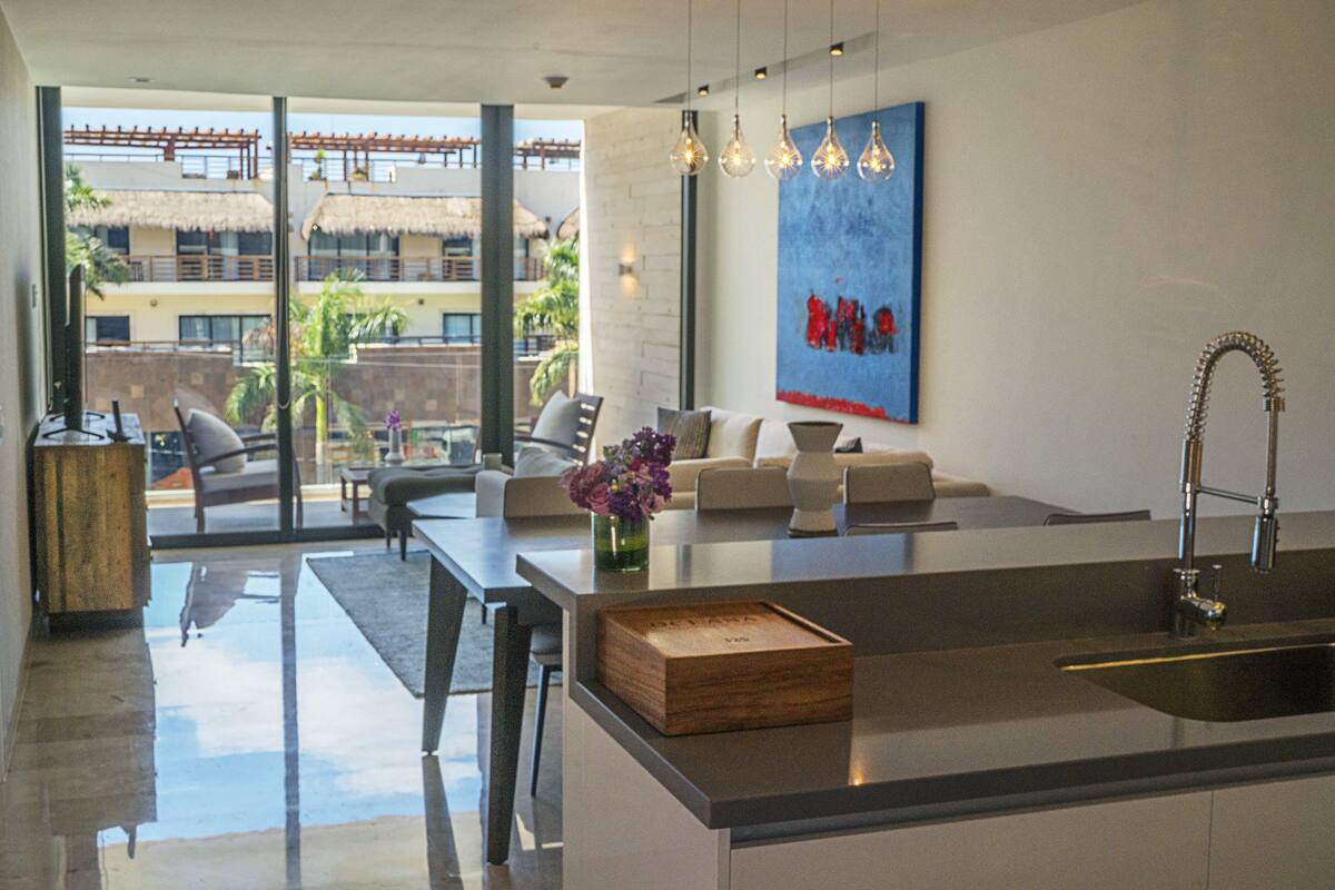 A modern kitchen with a large island, a dining area with a glass wall, and a living room with a sofa and a coffee table.