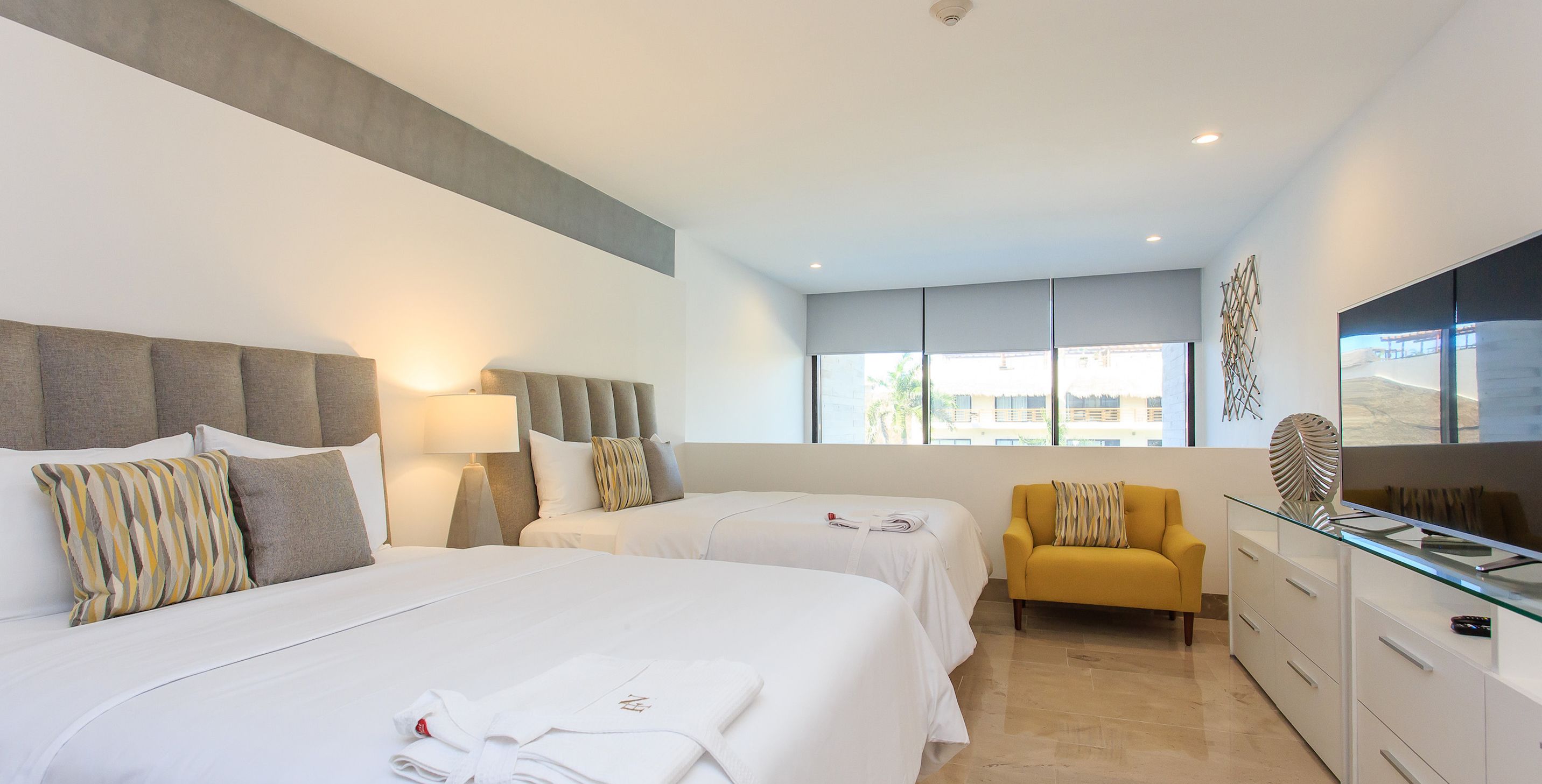 Een hotelkamer met twee bedden, een bank, een televisie en een groot raam.