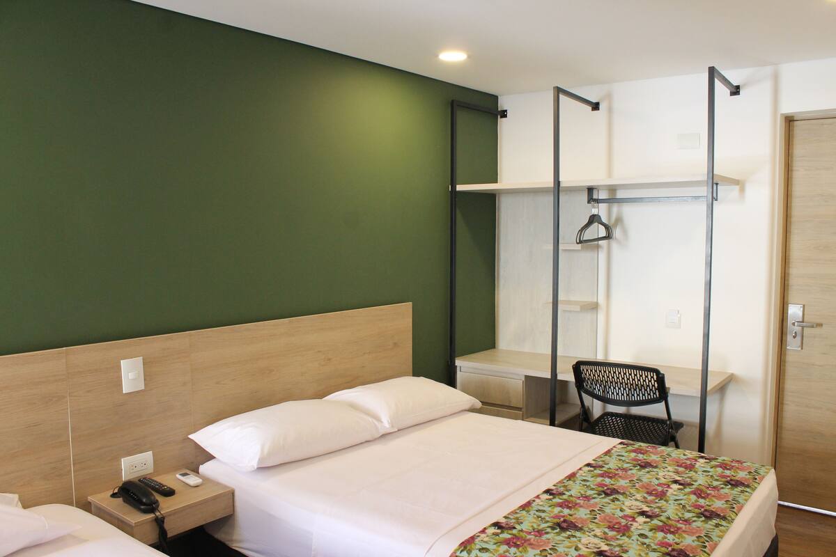 A hotel room with a bed, a desk, a chair, and a shower area.