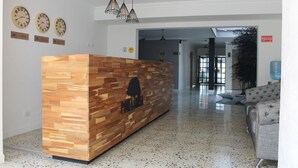 A reception desk with a wooden finish and a logo, a speckled floor, and clocks on the wall. - Hotel Poma - Rosa (Medellín)