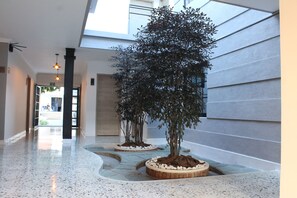 Corredor moderno de hotel com piso de terrazzo polido, claraboia e fileira de árvores em vasos.