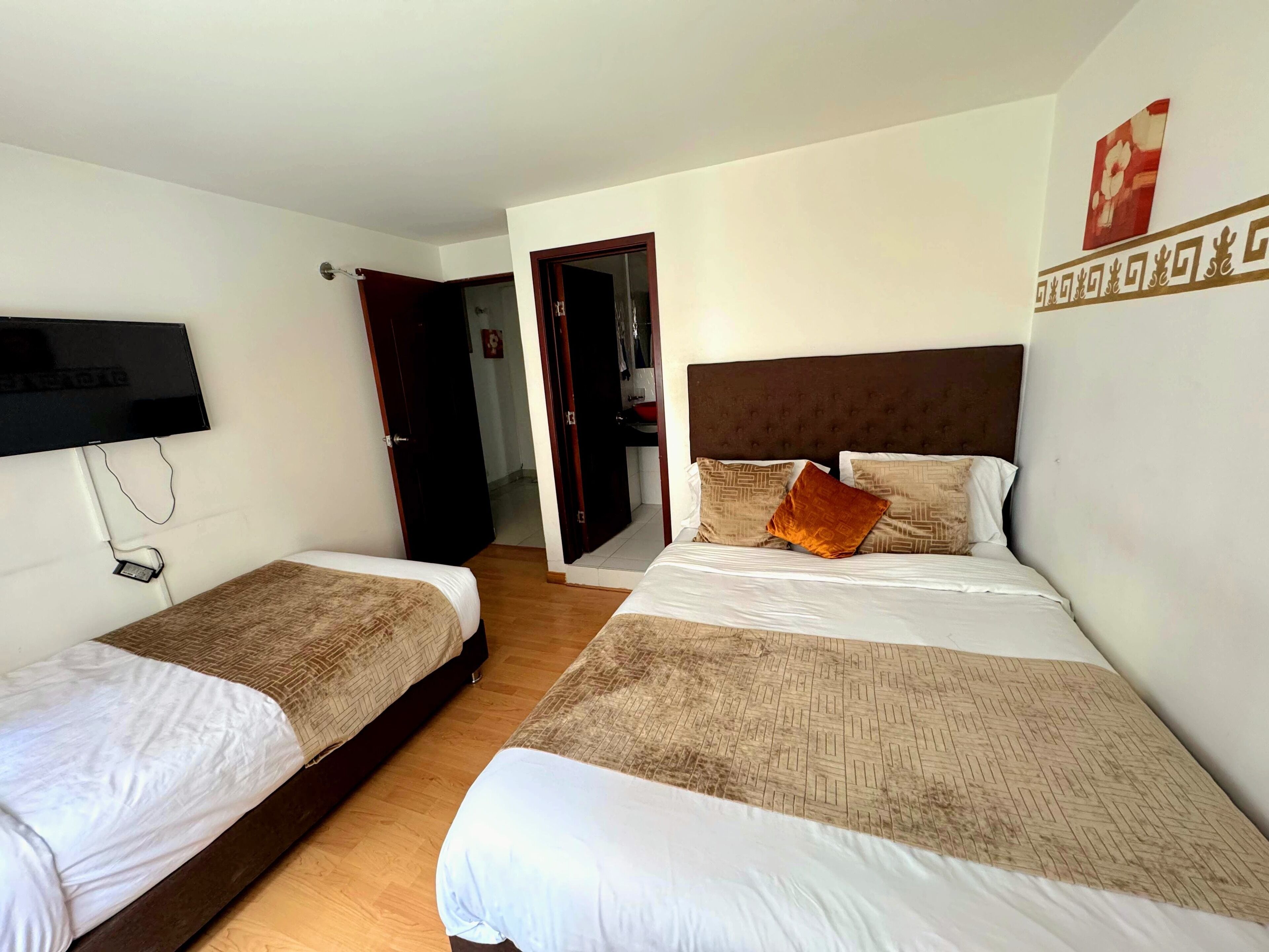 A hotel room with two beds, a TV mounted on the wall, and a door leading to another room.