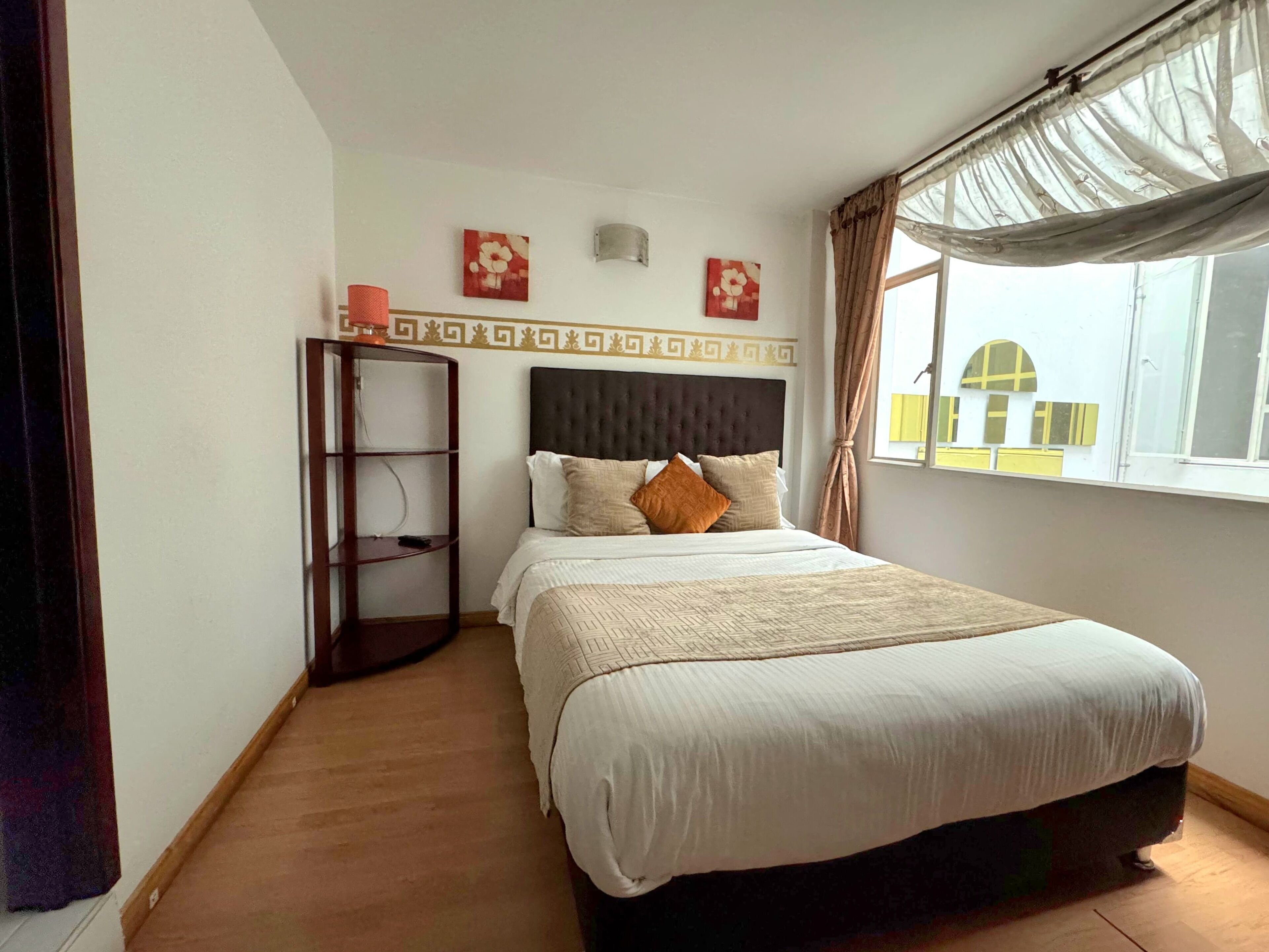 A bedroom with a bed, a nightstand, a shelf unit, and a window with curtains.