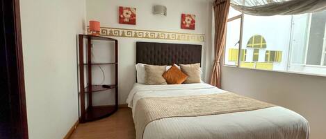 A bedroom with a bed, a nightstand, a shelf unit, and a window with curtains.