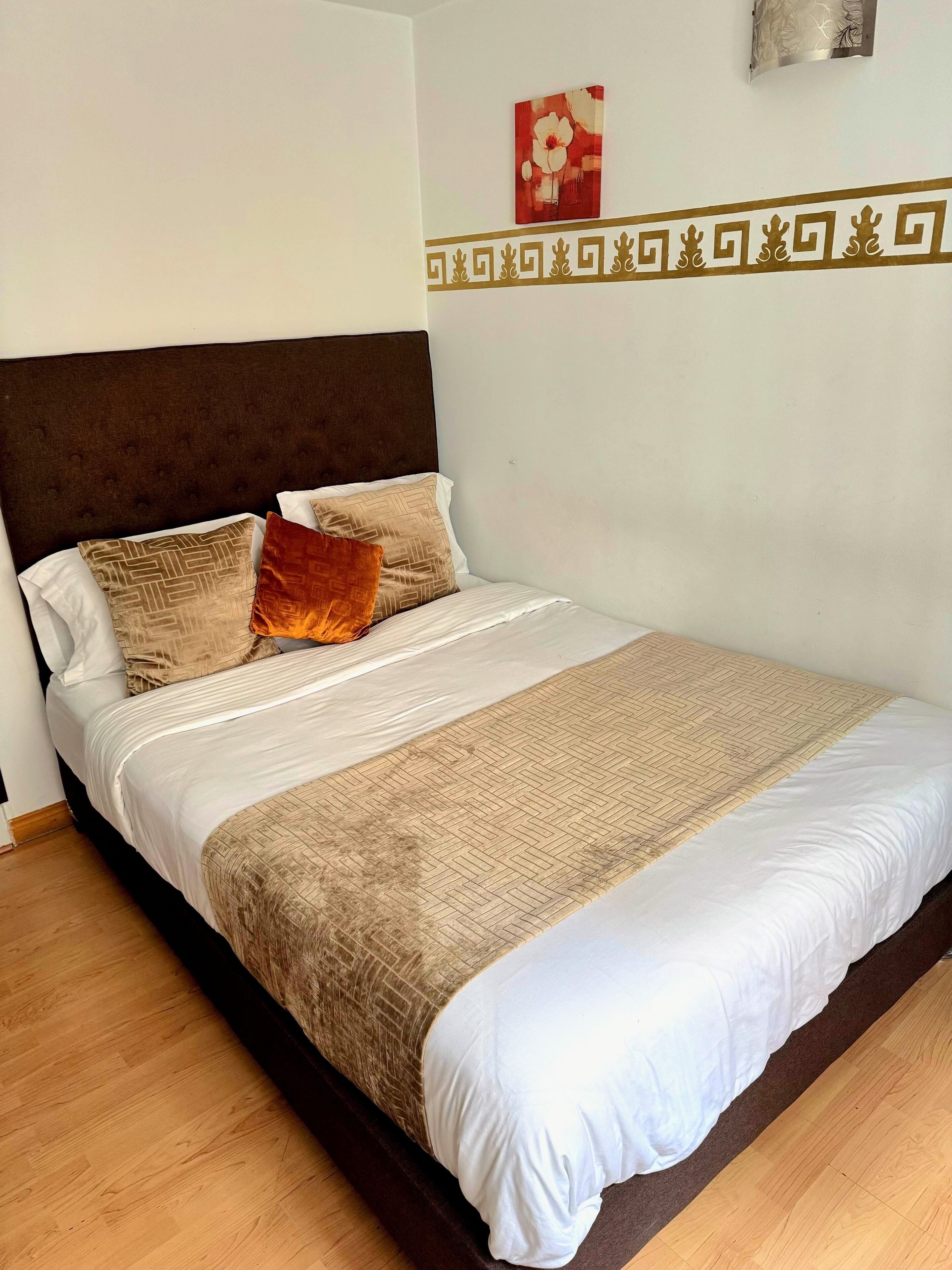 Un lit bien fait, avec une tête de lit marron, des oreillers blancs à motifs et une couverture beige.