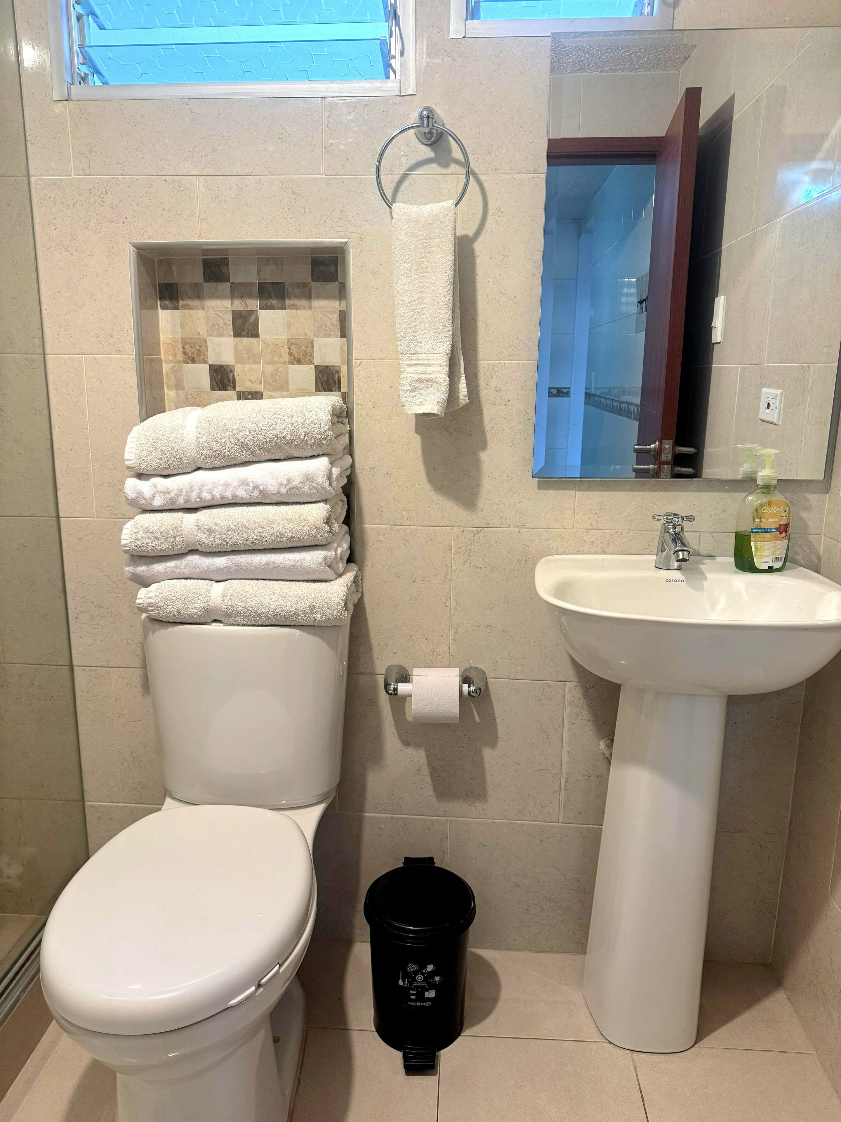 A bathroom with a toilet, a sink, a mirror, and a trash bin.