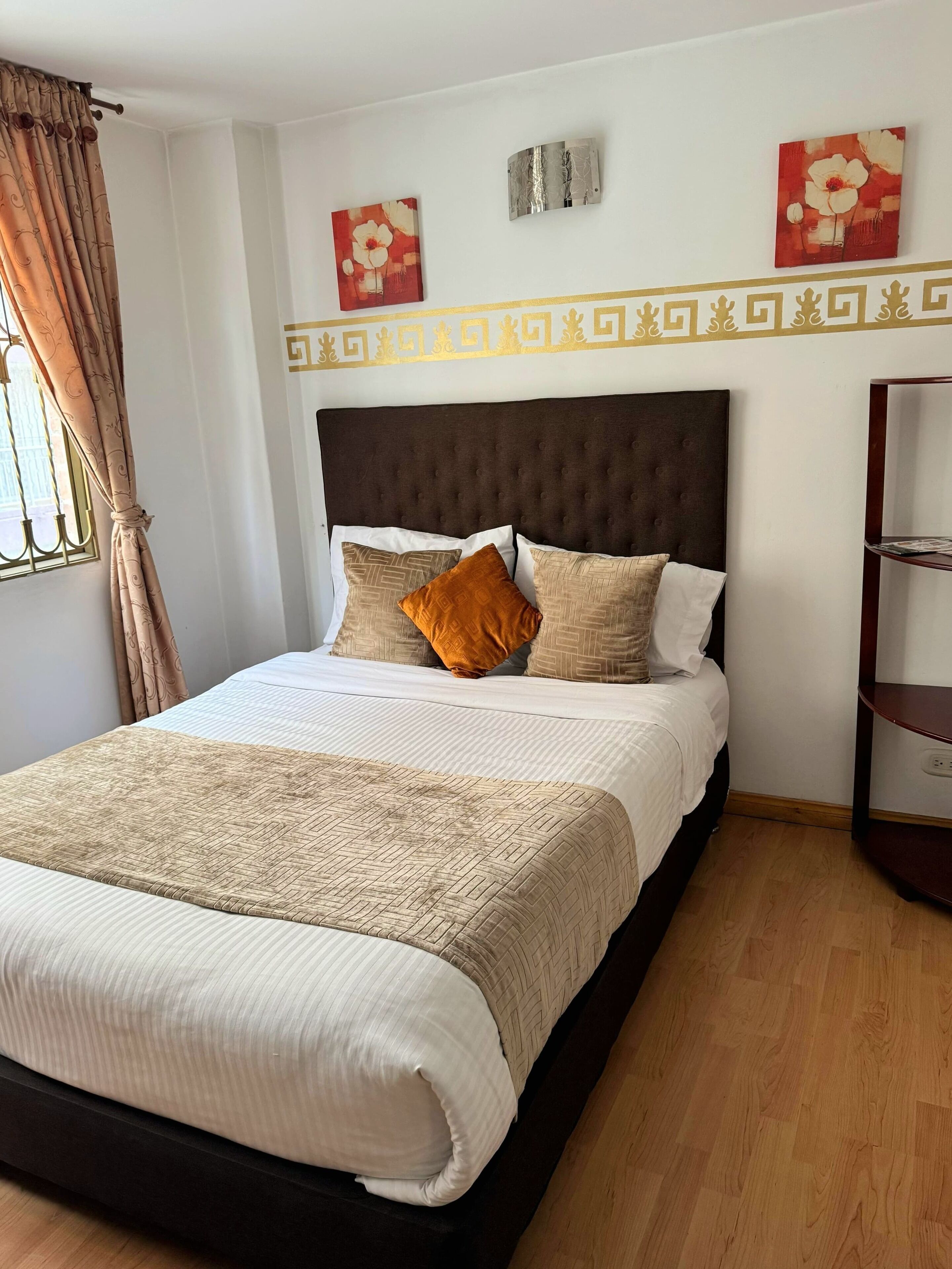 Cama bem arrumada com colcha estampada e almofadas, cabeceira escura e parede decorativa com padrão geométrico.