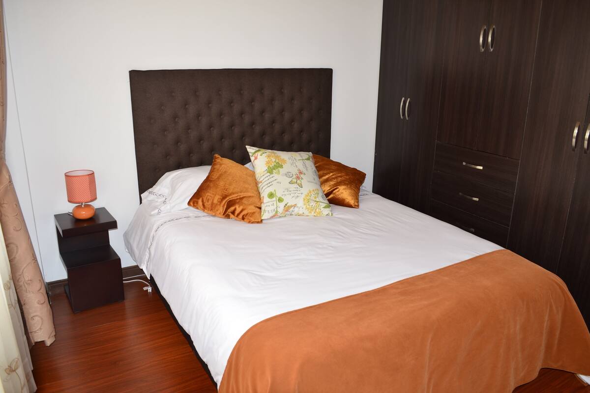 A bedroom with a large bed, a nightstand, a lamp, and dark wooden wardrobe.