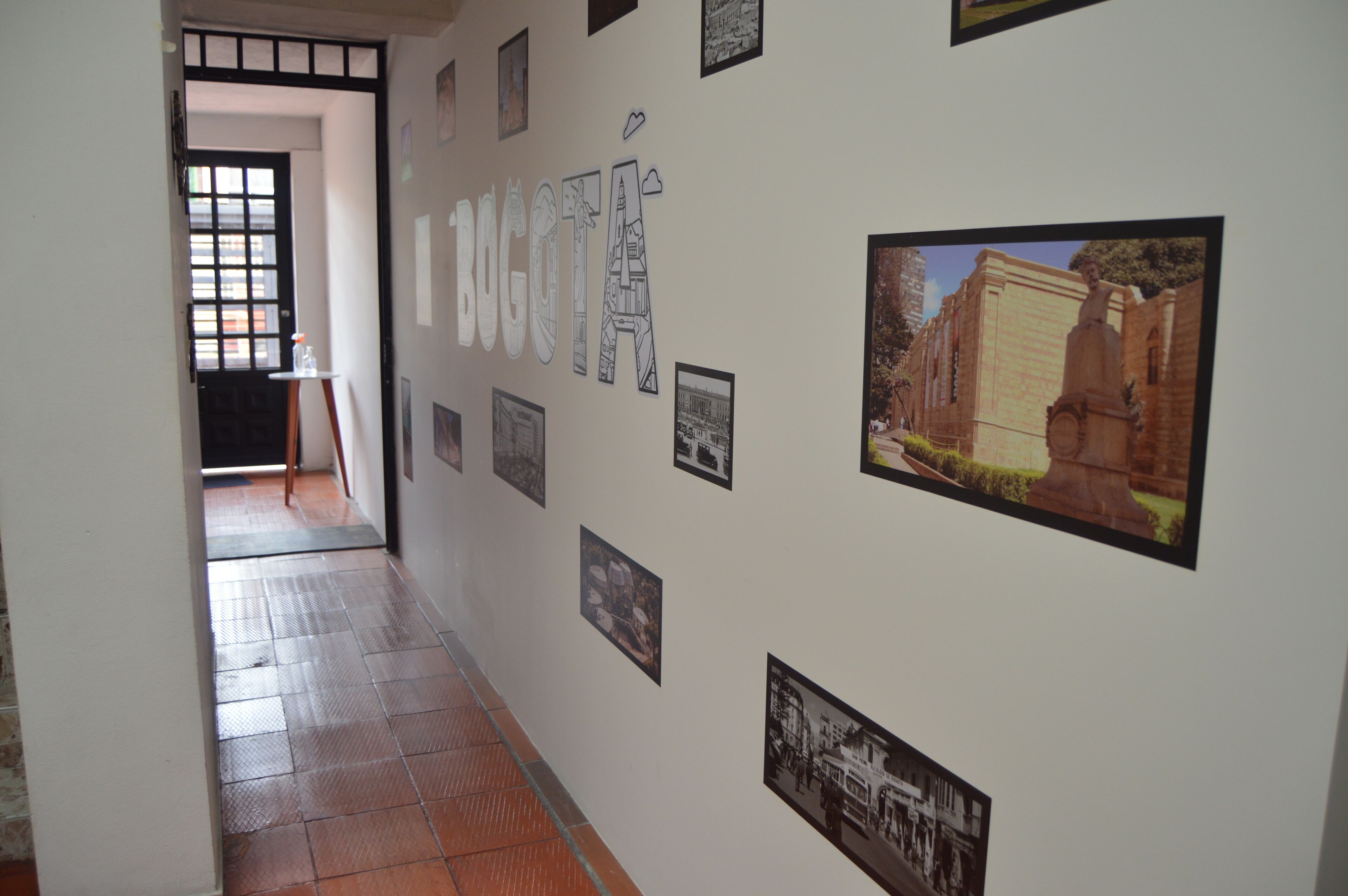 A hallway with a tiled floor, a black door, and a wall adorned with framed photographs and a large text sign.
