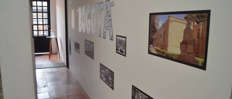 A hallway with a tiled floor, a black door, and a wall adorned with framed photographs and a large text sign.