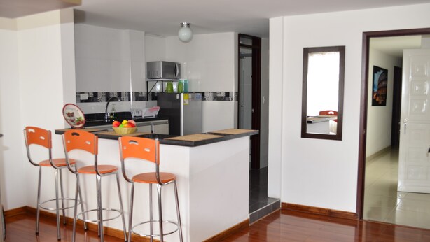 Una cocina moderna con una isla central, taburetes de bar y un microondas.