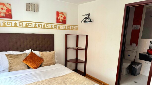 Una habitación de hotel ordenada con una cama grande, una mesita de noche, un espejo y un estante pequeño.