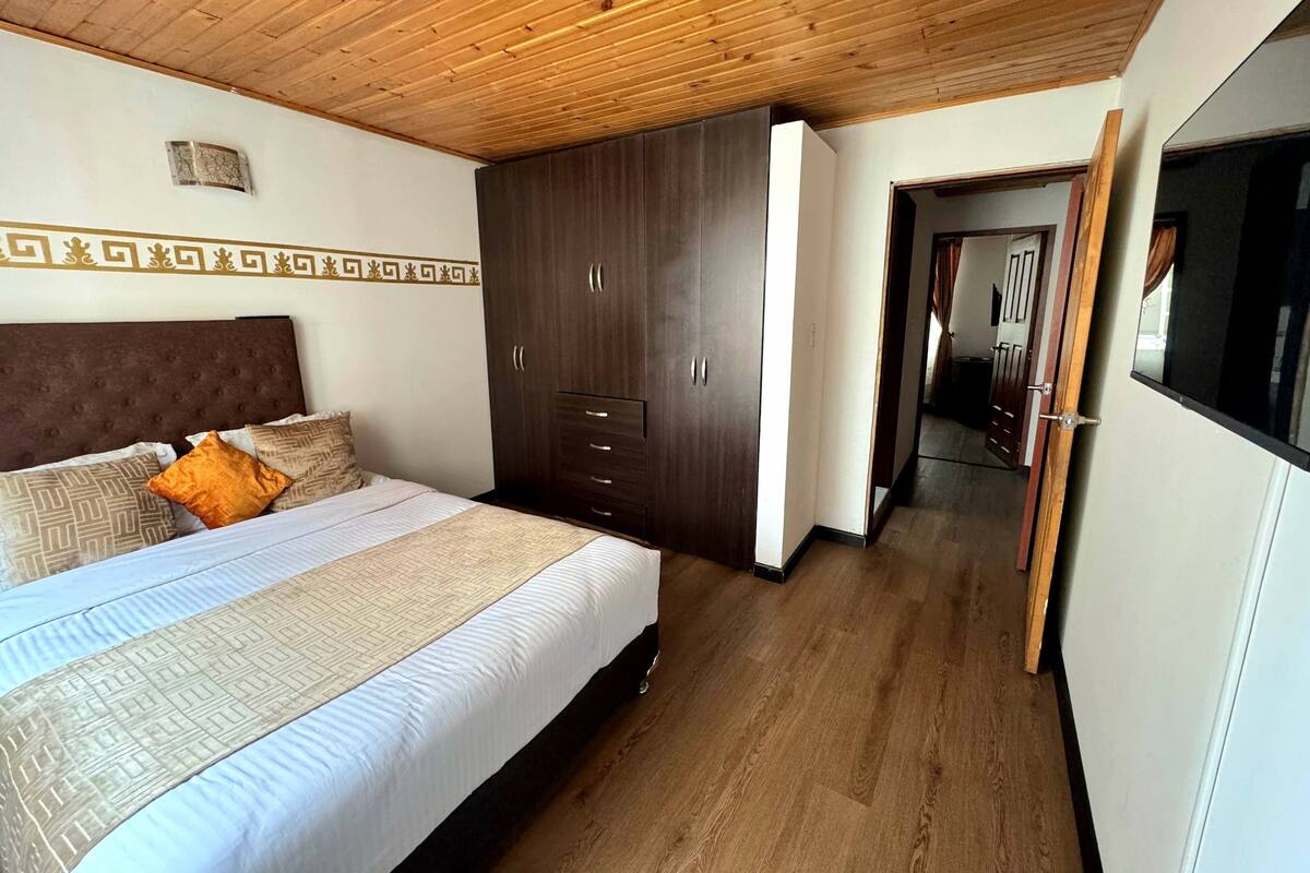 A bedroom with a bed, wooden wardrobe, and a hallway leading to another room.