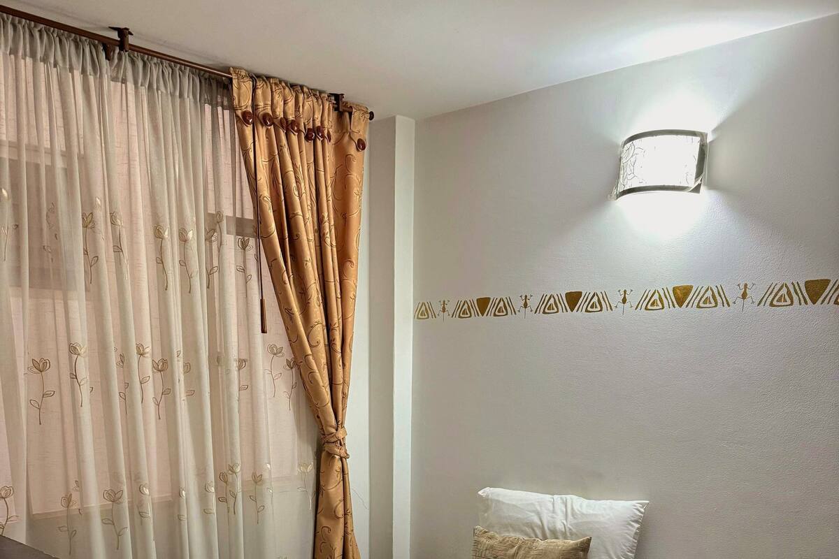 A neatly made bed with white linens and a patterned throw, a bedside table, and a wall-mounted light fixture.