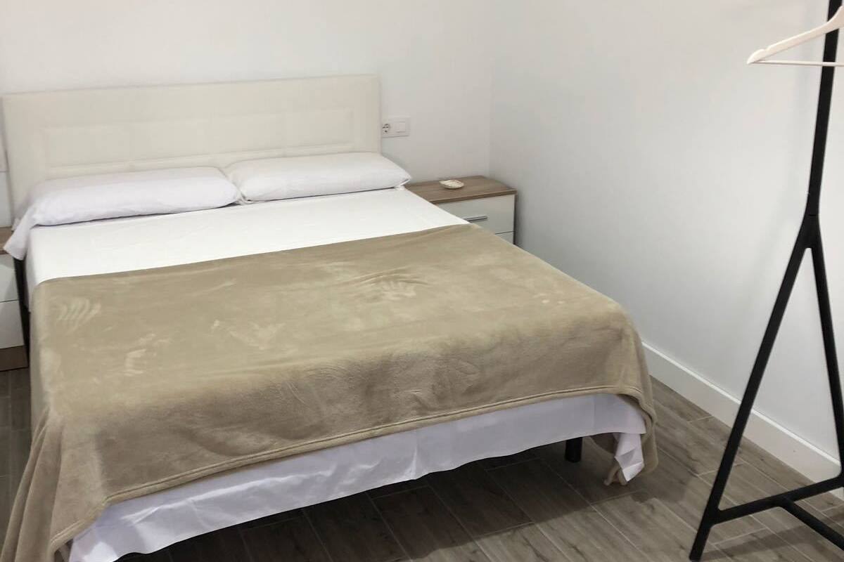 A neatly made bed with a beige blanket, a white pillow, and a wooden nightstand with a small lamp.