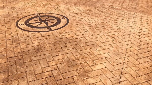 A rooftop terrace with a compass design on the floor, surrounded by white walls and trees in the background.