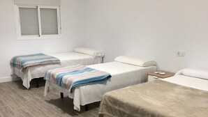 A room with three single beds, a small table, and a window with blinds.