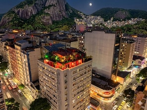 Un immeuble de grande hauteur, doté de nombreux étages, d’un jardin sur le toit et offrant une vue sur un paysage urbain, avec une montagne imposante en arrière-plan.