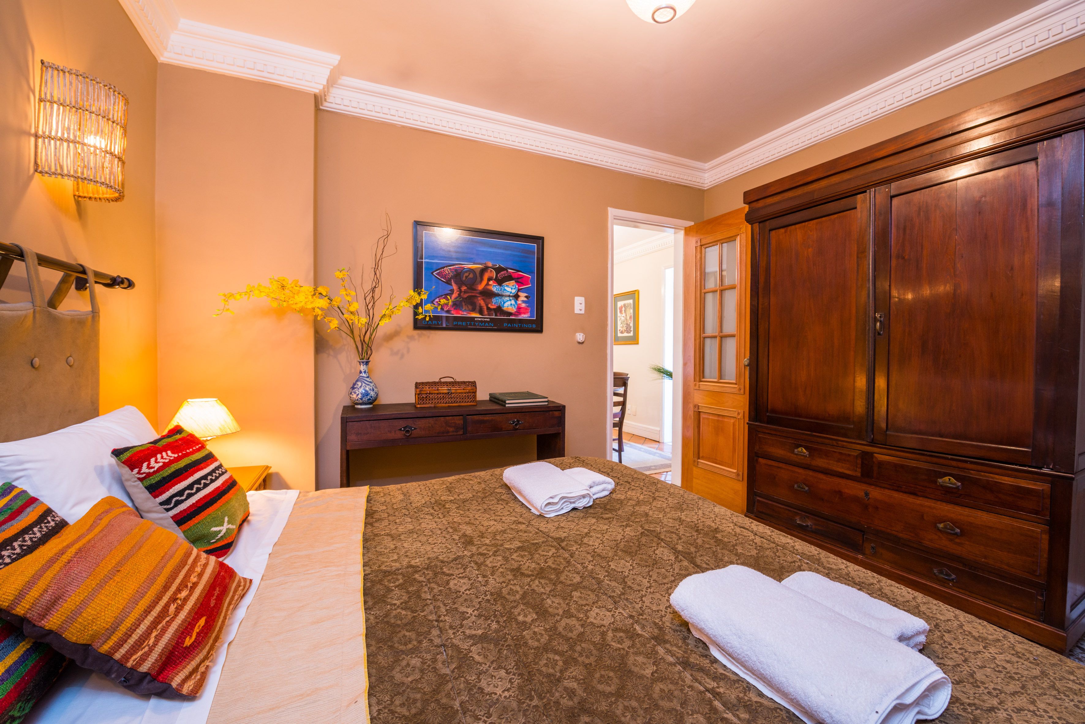 Een hotelkamer met een bed, nachtkastje, lamp, kast en een schilderij aan de muur.