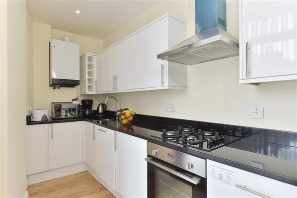 A modern kitchen with white cabinets, a black countertop, a gas stove, and a built-in oven. - Chancery Lane Apartments (London)