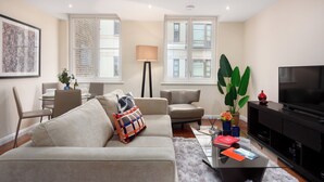 A modern living room with a sofa, armchairs, a coffee table, a TV, and a dining area with chairs and a table. - Chancery Lane Apartments (London)
