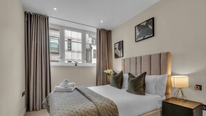 A hotel room with a large bed, a bedside table with a lamp, and a window with curtains. - Chancery Lane Apartments (London)
