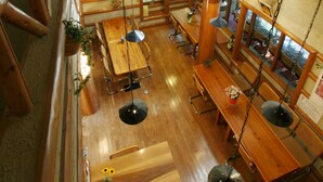 Un interior espacioso de madera con techos altos y vigas a la vista, que incluye varias mesas de madera y lámparas colgantes.